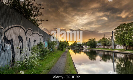 Spektakulären Sonnenuntergang über einem ruhigen Kanal, mit Graffiti bedeckt Wand im Vordergrund, und der Himmel im Wasser reflektiert Stockfoto