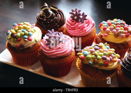 Nahaufnahme der eine Platte von Cupcakes dekoriert mit Mini Smarties und Schokolade und besprüht und Zucker Blumen Stockfoto