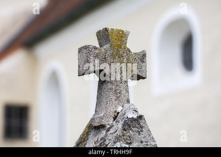 Nahaufnahme eines alten steinernen Kreuz. Die Wände und Fenster einer Kirche kann im Hintergrund gesehen werden. Religion, Gott, Christentum. Stockfoto