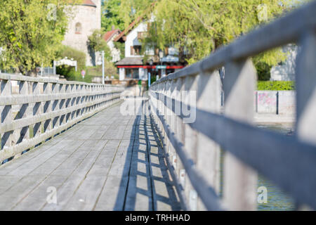 Low Angle View von einem Bootssteg/Pier am Ammersee. In Richtung Land. Holz Handlauf auf der linken und der rechten Seite. Bäume und Häuser im Hintergrund. Stockfoto