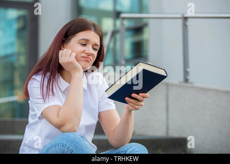 Demotiviert Schüler sitzen auf dem Campus Treppe, die versuchen, auf die Kamera zu studieren. Schüler lernen zu viel Aufgaben betonte Gefühl müde und gelangweilt. Stockfoto