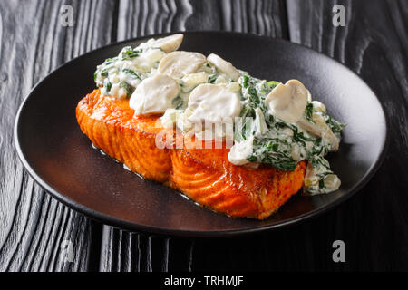 Bio Gebackenes Lachsfilet garniert mit cremigem Spinat, Knoblauch und Pilzen close-up auf einem Teller auf den Tisch. Horizontale Stockfoto