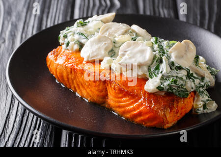 Gebackene Florentiner Lachs mit cremiger Wein Sauce, gewürzt mit gebratener Spinat und Pilze auf einem Teller auf den Tisch closeup. Horizontale Stockfoto