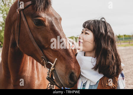 Süße chinesische Cowgirl, während die Pflege von Ihrem Pferd auf einem Wild West Farm Stockfoto