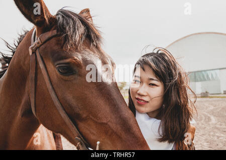 Süße chinesische Cowgirl, während die Pflege von Ihrem Pferd auf einem Wild West Farm Stockfoto