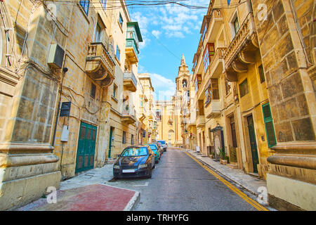 Die schmale Straße mit alten Wohngebiet edifises wnds mit Seitenwand von St Publius Pfarrkirche, Floriana, Malta gesäumt. Stockfoto