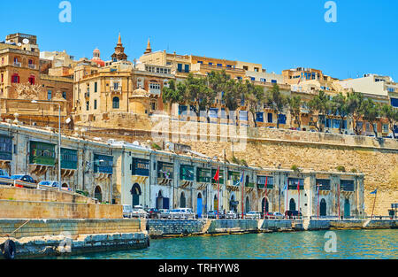 Die Linie des alten Lagerhallen und Bootsgaragen entlang Barriera Wharf vor der hohen Stadtmauer von Valletta, Malta. Stockfoto