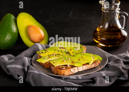 Teller mit leckeren Sandwiches mit Scheiben von frischen Avocado und Gewürzen auf Handtuch in die Küche platziert Stockfoto