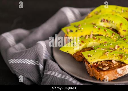 Teller mit leckeren Sandwiches mit Scheiben von frischen Avocado und Gewürzen auf Handtuch in die Küche platziert Stockfoto