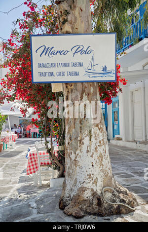 Restaurant Marco Polo zeichen Nagel zu einer Bougainvillea Baum, auf einer Art engen gepflasterten Straße in Mykonos mit Café im Freien. Stockfoto