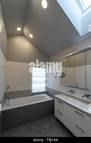 Bad im Dachgeschoss. Badewanne, Schrank mit Spülbecken und zwei Wasserhähne, Spiegel, Fenster und des Schiebedachs. Stockfoto
