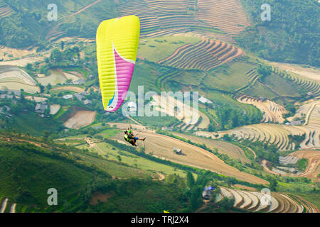 MU CANG CHAI, VIETNAM - 26. MAI 2019: Touristen Paragliding über Reisterrassen gewässert. Dies ist eine sehr berühmte Ort für Paragliding in Nordvietnam. Stockfoto