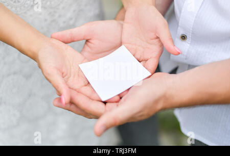 Ein kleines, leeres weißes Stück Papier liegt in den Händen von Männern und Frauen Stockfoto