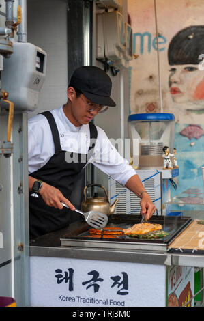 Junger Mann Anbieter kochen Pfannkuchen Buchimgae oder Koreanisch, Koreanisch traditionelles Essen, an einer Garküche in Gamcheon Culture Village in Busan, Südkorea Stockfoto