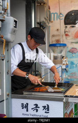 Junger Mann Anbieter kochen Pfannkuchen Buchimgae oder Koreanisch, Koreanisch traditionelles Essen, an einer Garküche in Gamcheon Culture Village in Busan, Südkorea Stockfoto