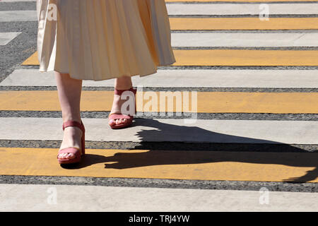 Frau, die in einem Sommer Kleid und Schuhe auf High Heels laufen auf Fußgängerüberweg, Schatten auf Zebra. Signalisieren, weibliche Beine auf dem Zebrastreifen Stockfoto