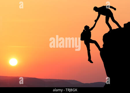 Jeder Teamarbeit paar Wandern helfen sie anderen vertrauen Hilfe Silhouette in Berge, Sonnenuntergang. Teamarbeit von zwei Männern, die Wanderer, die sich gegenseitig helfen auf mounta Stockfoto