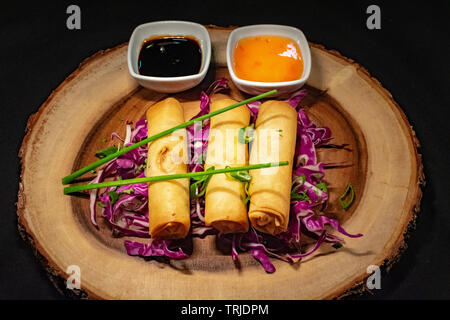 Ein Trio von Garnelen Frühlingsrollen auf einem Bett von Rotkohl mit einer Auswahl an Soßen zum Dippen begleitet Stockfoto