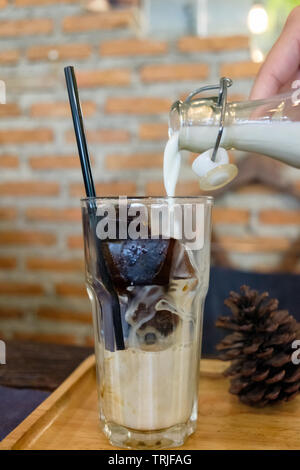 Eis Kaffee Cubes mit Milch Gießen in Glas in Retro Cafe Stockfoto