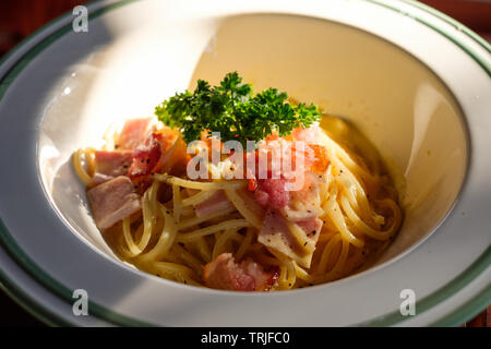 Spaghetti Carbonara mit Speck, Schinken und Gemüse in weiße Schüssel bei Sonnenuntergang Stockfoto