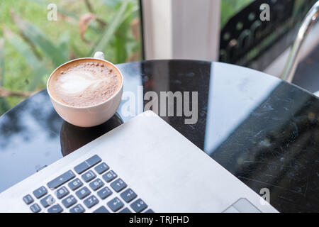 Laptop mit Latte heißen Kaffee in weißen Schale auf Glas Schreibtisch Stockfoto