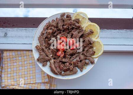 Rindersteak Schichten mit Tomaten und Zitronen in Scheiben geschnitten auf weißen Teller auf dem Tisch Stockfoto