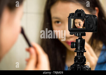 Fokus auf live view auf Kamera auf Stativ, junges Mädchen mit Kosmetik Bild zurück Bild mit unscharfen Szene im Hintergrund. Teenage vlogger livestrea Stockfoto