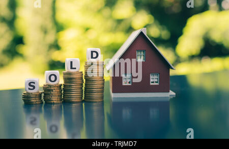 Konzept für den Verkauf eines Hauses. Würfel Form das Wort "Alt" auf die Steigerung der hohen Stapel von Münzen neben einem Modell Haus. Stockfoto