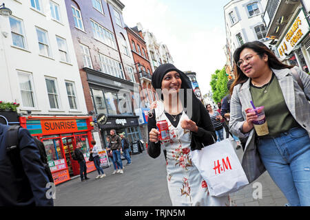 Junge Frauen gehen, reden und shoppen mit H&M Einkaufstasche auf der Gerrard Street in Chinatown London W1 England Großbritannien KATHY DEWITT Stockfoto