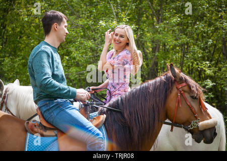 Schöne Mädchen in der Link geblümten Kleid und der junge Mann zu Fuß auf Pferde auf die Natur. Lifestyle Stimmung. Datum Liebhaber auf dem Pferderücken Stockfoto