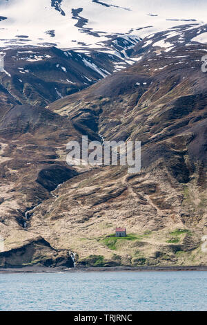 Húsavík, North Island. Ein einsames Bauernhaus am Ufer der Bucht Skjálfandi (Skjálfandaflói), unterhalb des schneebedeckten Bergrücken von die Víknafjöll Stockfoto