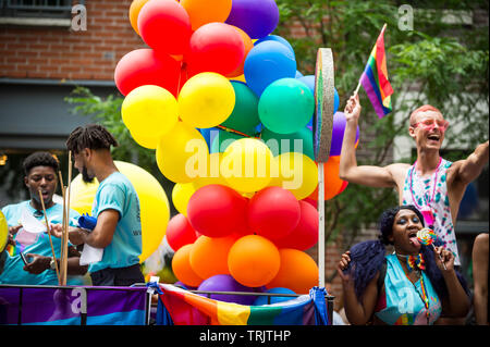 NEW YORK CITY - 25 Juni, 2017: Teilnehmer wave Regenbogenfahnen auf einem Schwimmer, der mit einem Ballon Bogen in die jährliche Gay Pride Parade in Greenwich Village. Stockfoto