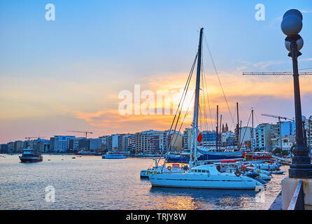 SLIEMA, MALTA - 19. Juni 2018: Die abendlichen Spaziergang entlang der Uferpromenade von Sliema mit Blick auf Linie der modernen Gebäuden, Segelyachten und die hellen Sonnenuntergang Stockfoto