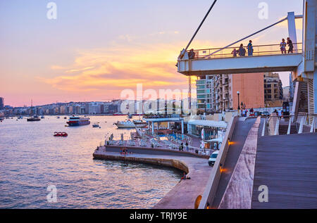 SLIEMA, MALTA - 19. Juni 2018: Die malerischen Abend in Resort mit Blick auf den Hafen mit Schiffen, feurigen Himmel und komfortable Küstenpromenade von Tign Stockfoto