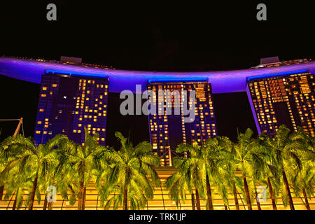 Marina Bay Sands Hotel, umgeben von Palmen und bei Nacht beleuchtet. Singapur Stockfoto