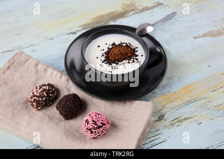 Schwarze Tasse Kaffee mit Milch. Woman's Hände, die Tasse mit Kaffee, Ansicht von oben. Stockfoto