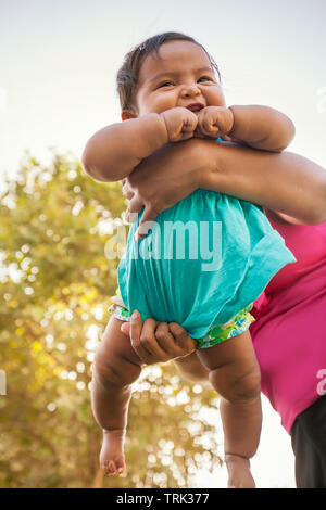 Ein fröhliches kleines Mädchen wird in der Luft durch die Mutter, die Ihr kräftige Gewicht ist die Unterstützung im Hintergrund schwang. Stockfoto