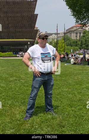 Washington, D.C., USA. 1. Juni 2019. Mit dem Nationalen Museum für Afrikanische Amerikanische Geschichte und Kultur im Hintergrund auf der linken Seite, ein muskulöser Mann in akimbo Haltung trägt ein t-shirt Lesen "Anzuklagen" mit einem Bild des Weißen Hauses, und ein Callaway Hex heißen Hut/Kappe, an der Nationalen März Anzuklagen am 1. Juni 2019, auf dem Washington Monument in Washington, D.C., USA, durch die Leute verlangen Aktion organisiert. Stockfoto