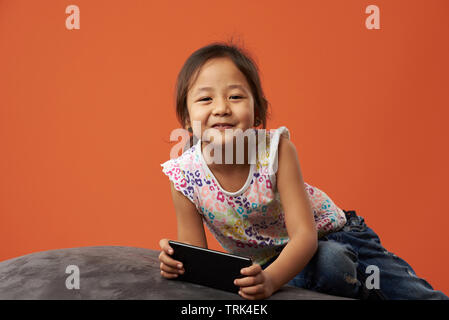 Asiatische Mädchen spielen mit Smartphone auf orange Farbe Hintergrund isoliert Stockfoto