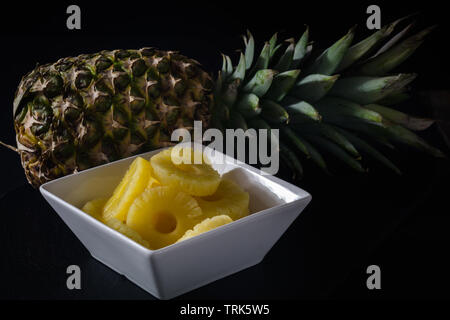 Ananas auf schwarzen Hintergrund. Mit runden reifen Stücke Ananas in einer weißen Schüssel. Stockfoto