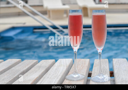 Ferienhäuser feier Konzept: Zwei Gläser mit rosa Champagner gefüllt. Schwimmbad von Kreuzfahrtschiff im Hintergrund. Stockfoto