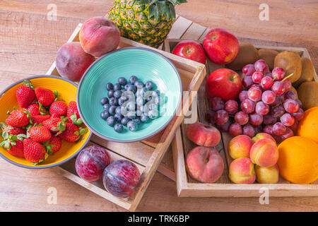 Zwei Kisten voll von bunten Früchte auf einem hölzernen Hintergrund. Enthält Ananas, Weintrauben, Äpfel, Kiwis, Orangen, Aprikosen, Blaubeeren und Erdbeeren. Stockfoto