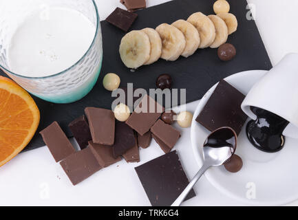 Teile der handwerklichen dunkle Schokolade, Chocolate Chips Banane ein Glas Milch isoliert. Horizontale Komposition. Ansicht von oben Stockfoto