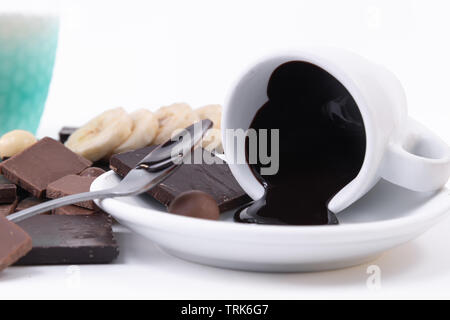Geschmolzene dunkle Schokolade mit einer cremigen Textur aus einer Tasse und einem Stück Schokolade verschüttet. Nahaufnahme Stockfoto