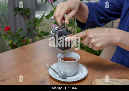 Winter tee Konzept. Frau Hände. Mädchen gießt Zitrusfrüchte Tee mit Zitronen und Orangen aus transparentem Glas Teekanne in eine Tasse. Stockfoto