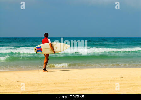 Junge Frau mit Surfbrett Spaziergänge an einem Sandstrand entlang dem Meer Stockfoto