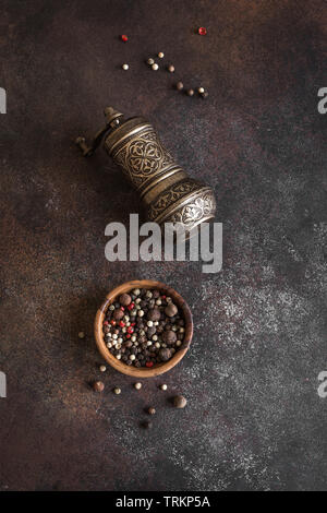 Vintage Pfeffer Mühle und gemischte Pfefferkörner auf dunklem Hintergrund. Kochen und orientalischen Gewürzen Konzept, Ansicht von oben. Stockfoto