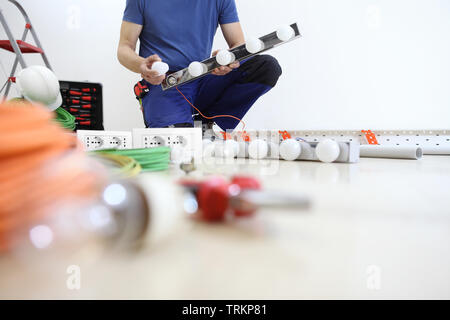 Elektriker am Arbeitsplatz installieren Lampe mit Glühbirne in der Hand, Einbau der elektrischen Stromkreise, elektrische Verkabelung Stockfoto