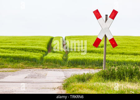 Unbewachten Bahnübergang mit saltire Zeichen an einsamen ländlichen Weg, keine Zug passiert, Grün landwirtschaftliches Feld im Frühling (Kopie) Stockfoto