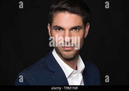 Eine gut aussehende weiße männliche Modell Modellierung in einen Anzug, ein Kopf und Schulter Portrait, dunklen schwarzen Hintergrund. Er blickt zuversichtlich. Stockfoto